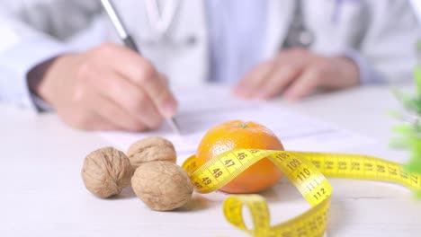 fotografía en primer plano de un nutricionista escribiendo una receta de dieta, nueces, mandarina y cinta métrica en la mesa