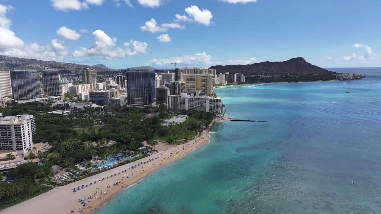 Aerial drone footage over Waikiki Beach in Honolulu, Oahu, Hawaii, featuring the iconic Diamond Head volcanic crater, turquoise ocean waters, palm trees, and luxury beachfront hotels along the coast