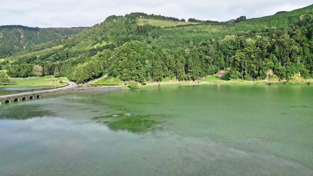 푸른 언덕은 나무와 다리로 둘러싸인 조용한 호수에서 반사됩니다.