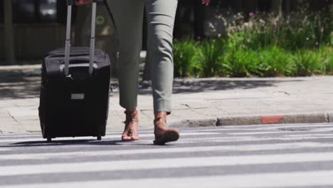 low section of african american woman crossing road wheeling suitcase