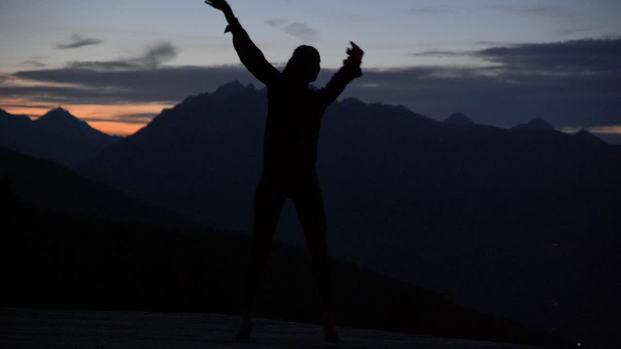 cámara lenta: hermosa foto de la silueta de una mujer joven bailando en una plataforma al atardecer en las montañas