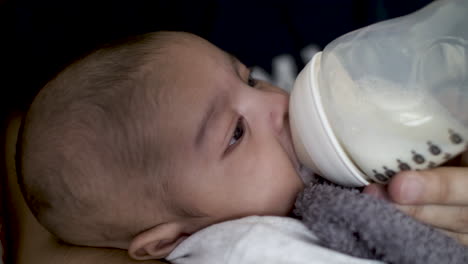 2 month old indian baby boy calmly drinking breast milk from bottle and fidgeting