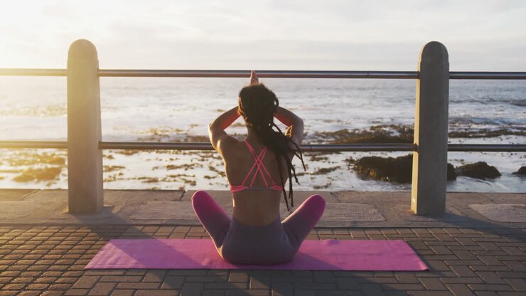 Vista trasera de mujer afroamericana practicando yoga en el paseo marítimo cerca del mar.