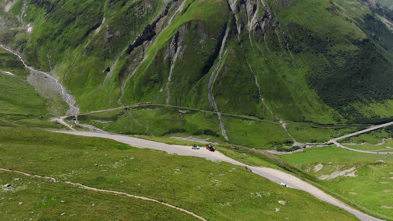 Furka Pass snakes through towering green Swiss Alps, breathtaking aerial footage