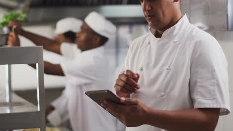 cocinero de raza mixta usando una tableta en la cocina de un restaurante