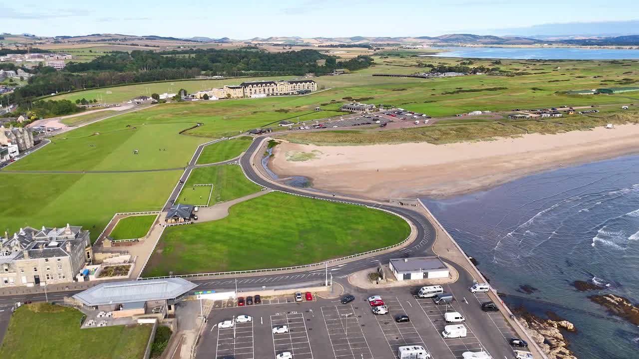 Aerial drone video gliding over historic golf course, Victorian buildings, and sandy coastline in Scotland
