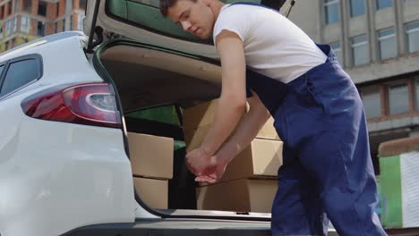 moving and delivery of manufactured goods. the assistant puts the cargo in the craft boxes in the trunk of the car and closes the car door. side view