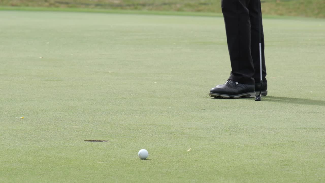 Golfer failed putting golf ball to hole on green golf course on hills in open tournament competition. Slow motion.
