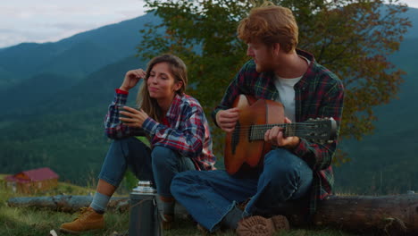 music couple sit camp in mountain landscape. carefree lovers play guitar outside