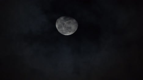 brillantes cráteres y crestas blancas de la luna se levantan en el cielo a medida que las nubes pasan por debajo por la noche