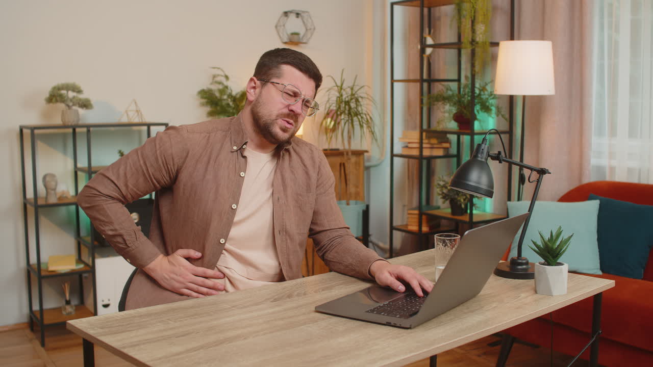 Disappointed freelancer man feeling stomach ache overeating during work process on laptop at home