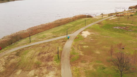 a bird's eye view over a person walking along a paved walkway, on a cloudy day in flushing meadows corona park, ny with meadow lake to their left, pt two