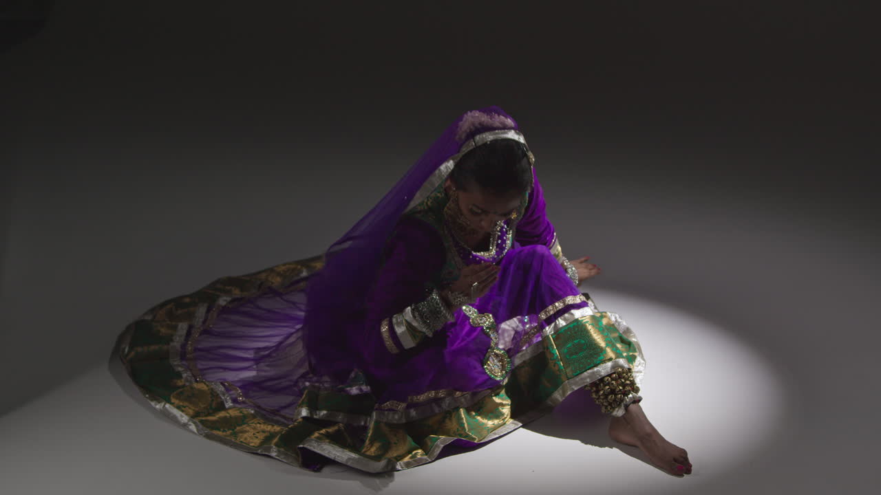 Female Kathak Dancer Performing Dance Wearing Traditional Indian Dress Seated On Floor In Spotlight 1