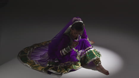 female kathak dancer performing dance wearing traditional indian dress seated on floor in spotlight 1