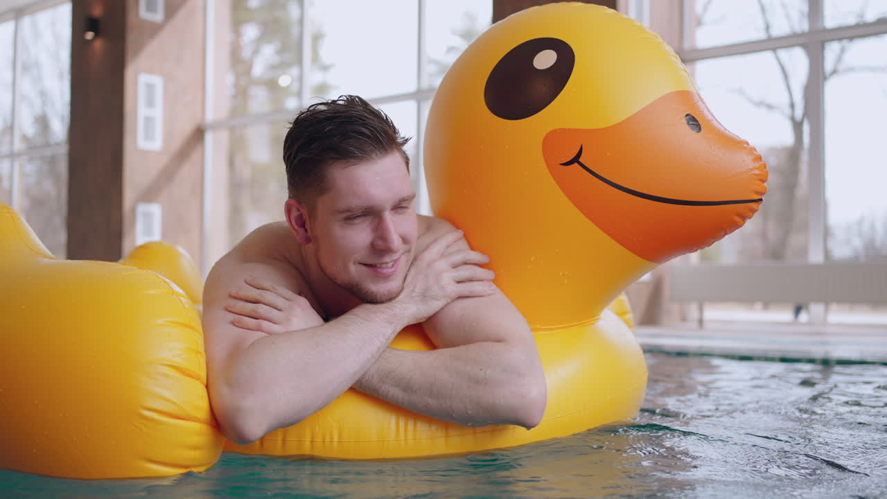 수영장 이나 온수 욕조 의 행복 한 남성 방문자 는 부풀어 올릴 수 있는 오리 초상화 에 떠 있다