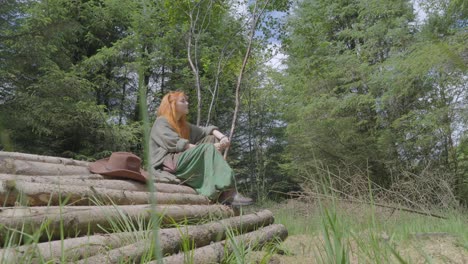 girl sat on log pile in forest clearing on sunny summer day low angle slow approach at half speed slow motion