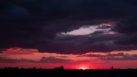 time lapse of beautiful scenic red sunset over the city with sun rays shining through the clouds, high contrast low fast moving clouds at summer evening, urban environment, wide shot