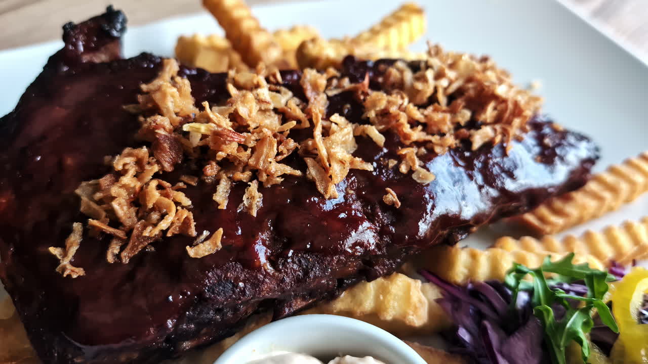 Juicy cooked meat topped with fried onions and rich sauce, served on a plate in a restaurant setting.