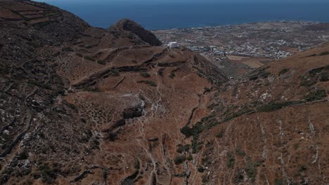 Aerial-view-approaching-a-church-in-the-highlands-of-Santorini,-sunny-Greece---tilt,-drone-shot