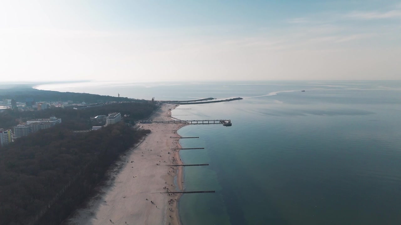 Ilmakuva laajasta hiekkarannasta, laiturista ja tyynestä merestä Kołobrzegissa.