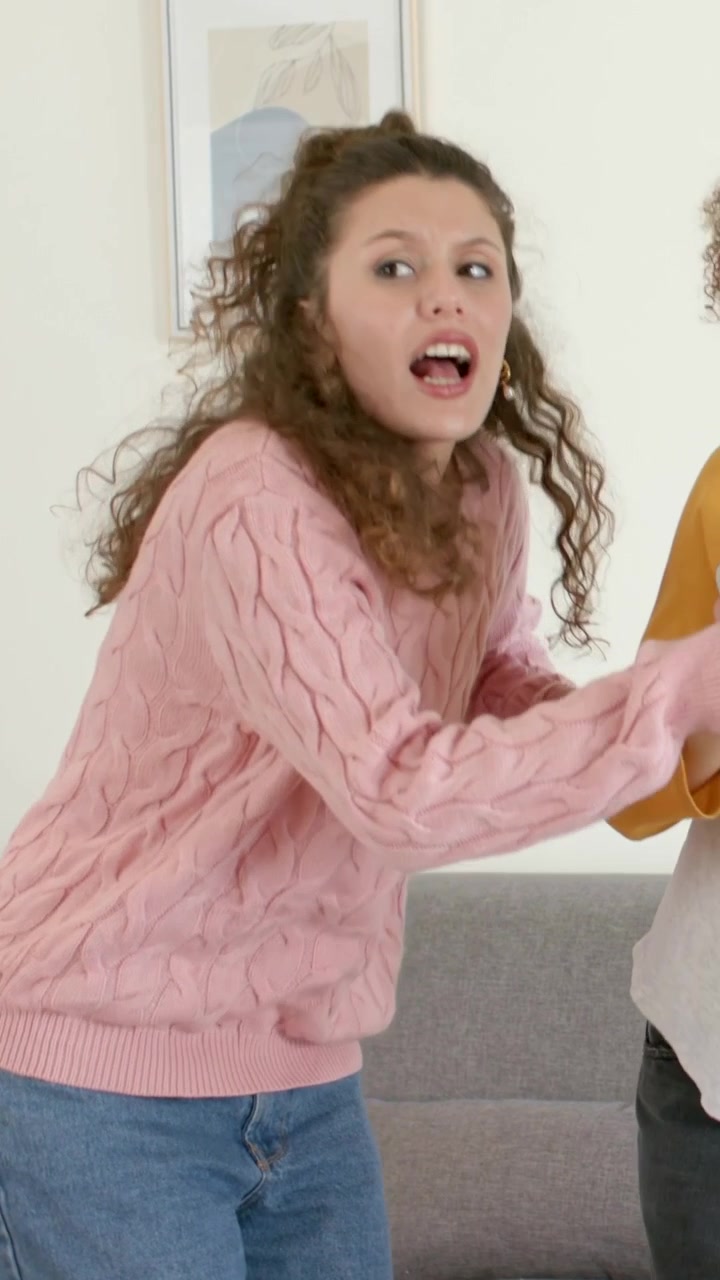 Vertical video: Grabbing mic from friend, woman in pink sweater singing at home, sharing song