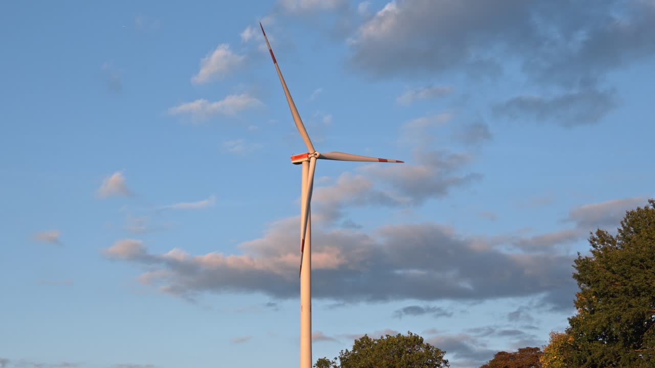 Modern onshore wind turbine silhouetted against a colorful, darkening sky at dusk in Germany