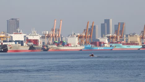 a small boat moves across a bustling port backdrop