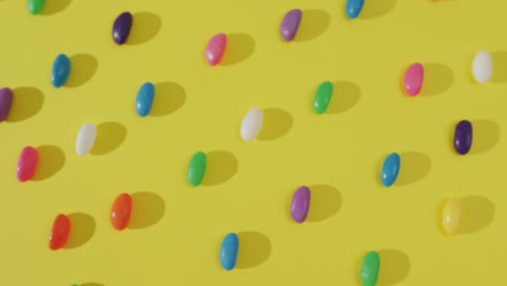 video of overhead view of rows of multi coloured sweets over yellow background