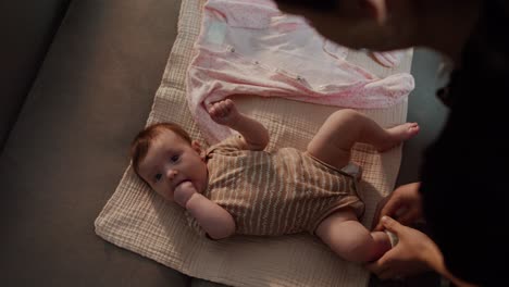 top view mom puts her little baby daughter on a special mat in a brown overalls and prepares clothes to change clothes on her little baby daughter