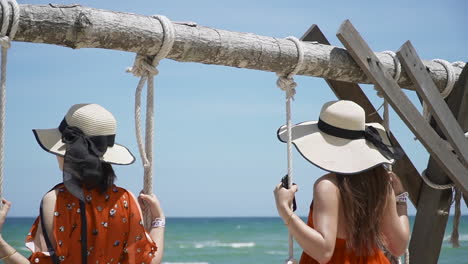 two girls sitting on swing at beach