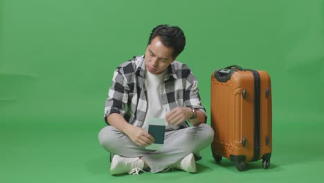 full body of asian male traveler with luggage and passport having a headache while sitting in the green screen background studio