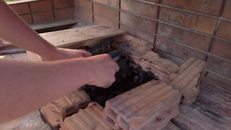 Slow-Motion-Wide-Shot-of-Man-Placing-Firelighters-into-Charcoal-to-Prepare-a-Greek-Style-BBQ-for-Cooking-at-Dusk