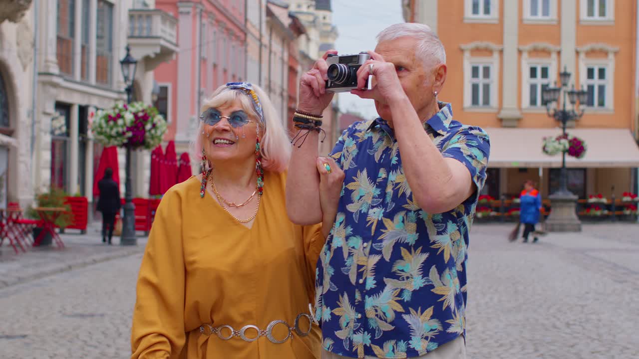 ancianos turistas elegantes hombre y mujer tomando fotos con vieja cámara de película, caminando por la calle de la ciudad