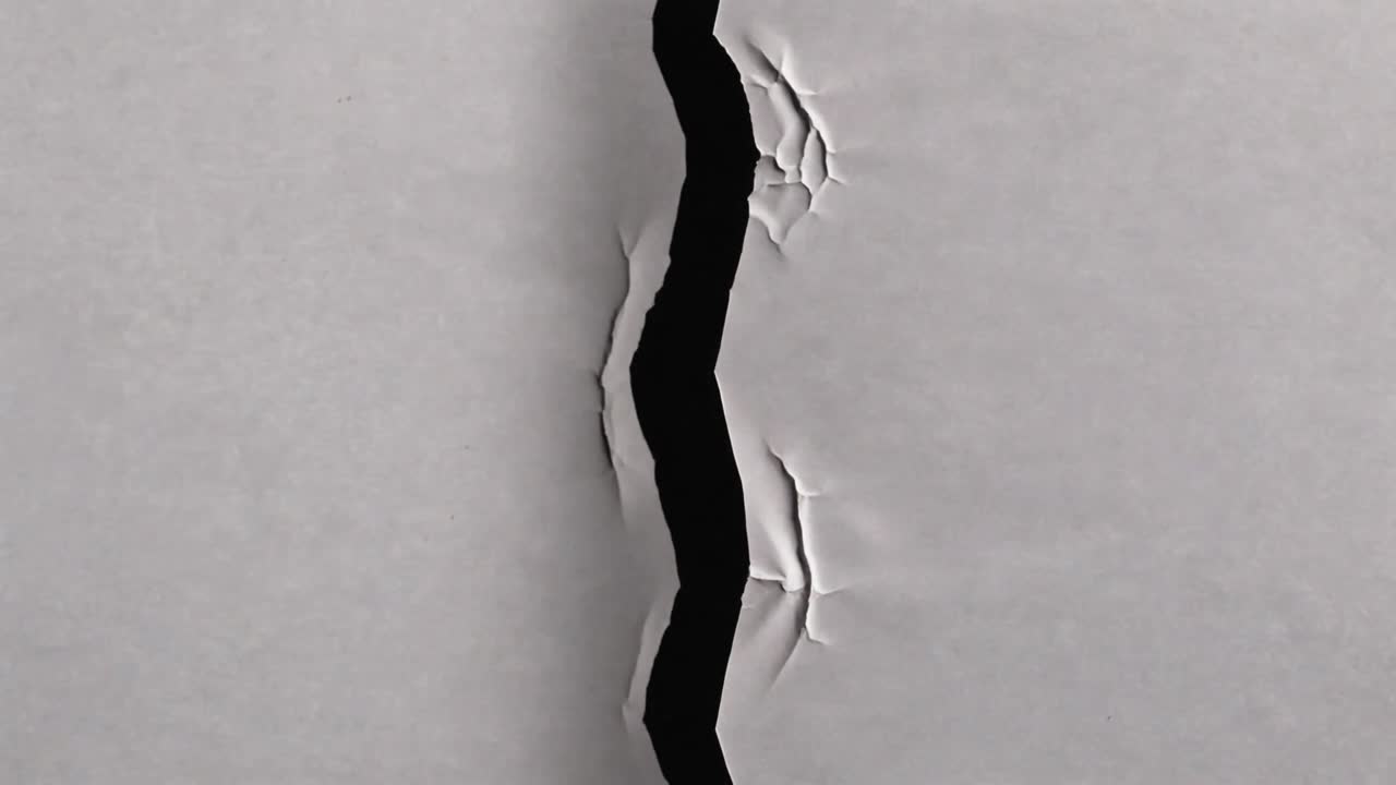 Revealing torn gap in gray sheet, curled edges and dark void widening under shifting studio light