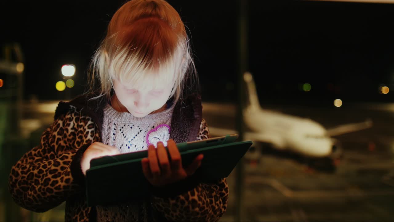 chica rubia jugando en la tableta en el aeropuerto temprano en la mañana en la terminal del aeropuerto