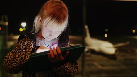 blonde girl playing on the tablet at the airport earlier in the morning at the terminal of the airpo