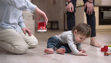 Baby-Sitzt-Auf-Dem-Boden,-Während-Seine-Mutter-Mit-Einem-Spielzeugauto-Spielt