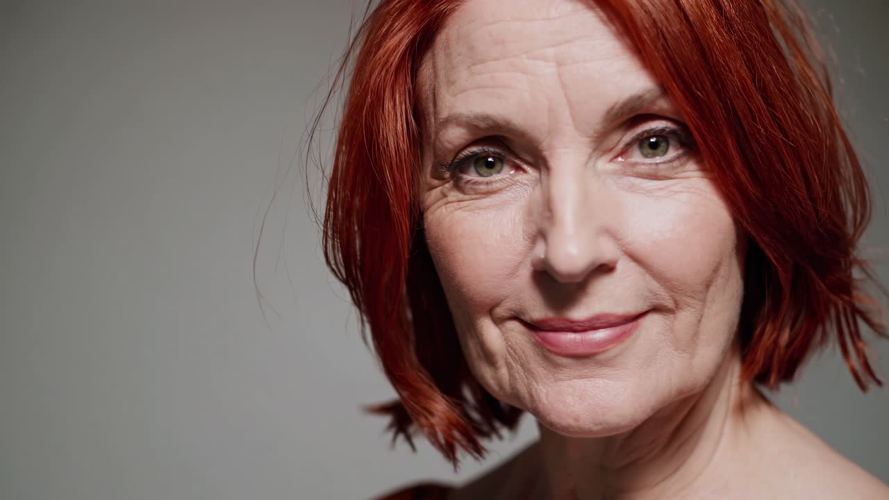 Confident and serene mature woman with radiant red hair and green eyes posing for a wellness and beauty portrait, embracing age with grace and showing a genuine smile