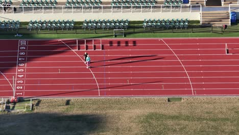 two athletes practice on an empty athletics track under bright daylight, focusing on sprinting and hurdling techniques