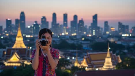 a joyful moment captured: a young woman smiling and holding a camera against a beautiful city skyline during twilight