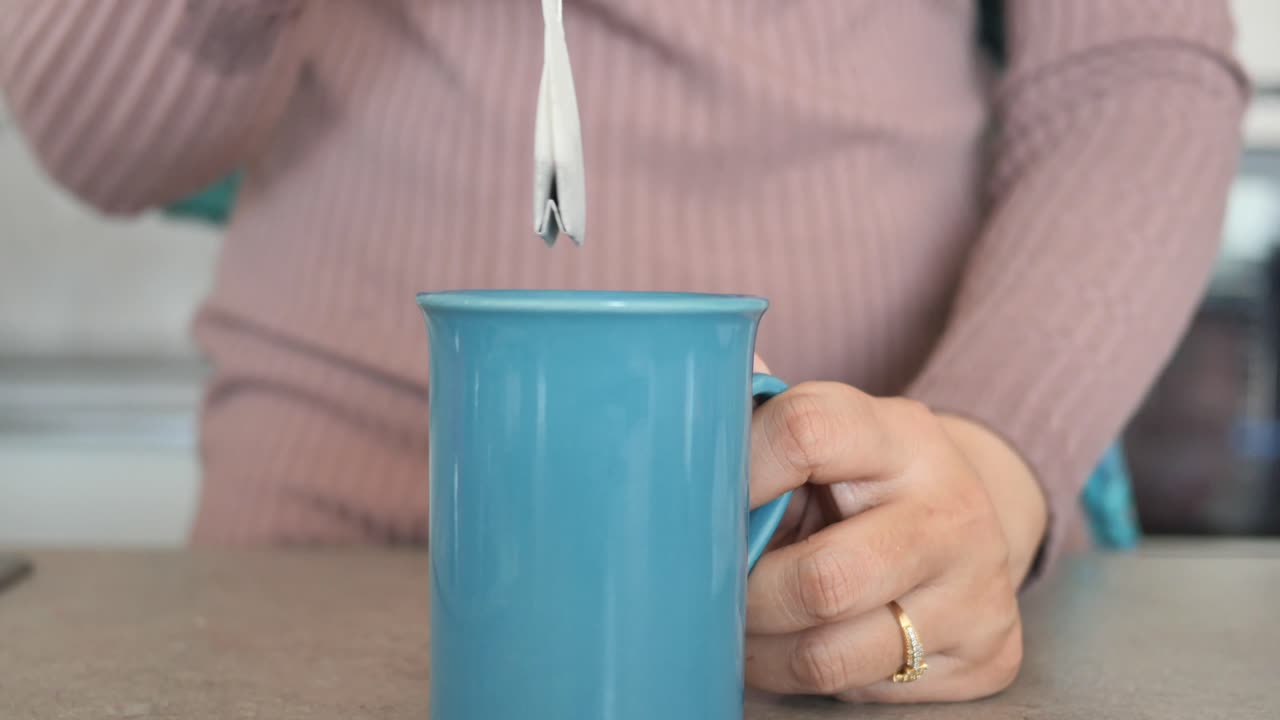 여자 는 차 가방 을 푸른색 컵 에 담고 있다