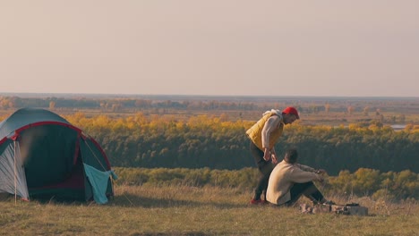 man in yellow vest comes to sad friend sitting at campfire