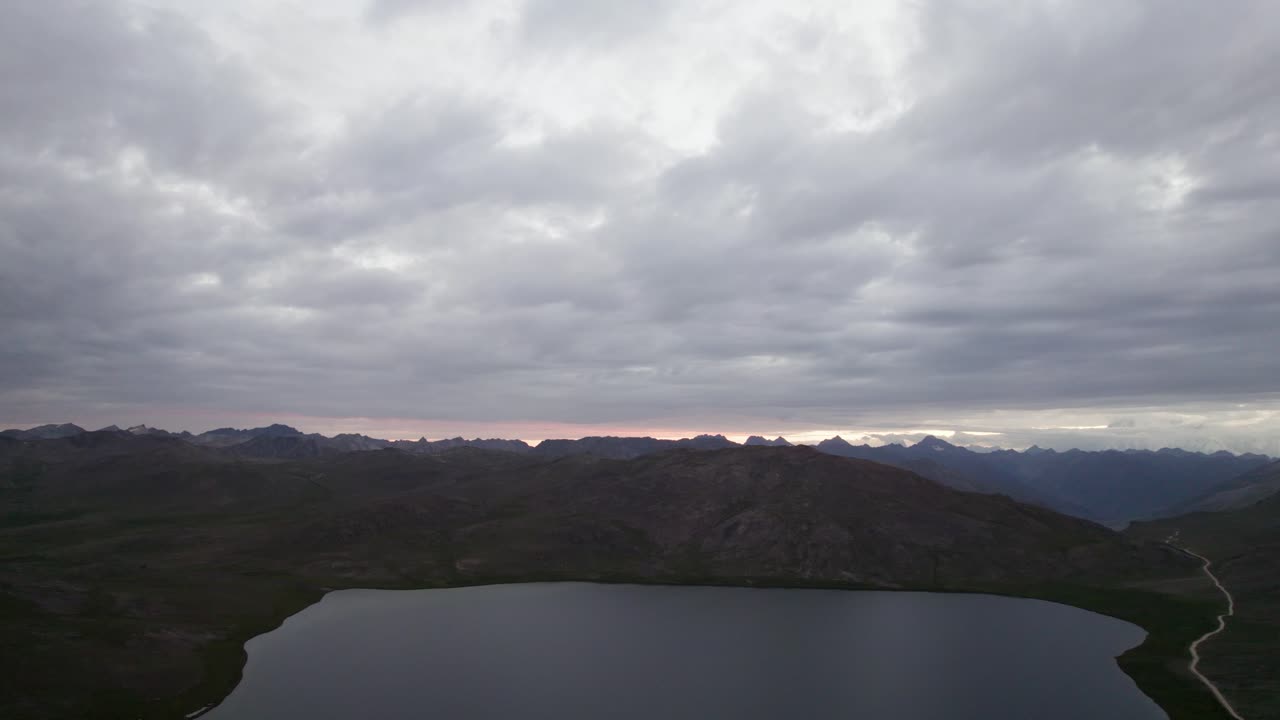 Dark clouds loom above Sheosar Lake with Himalayan peaks in the background at Deosai National Park