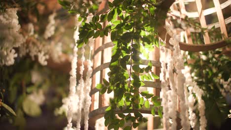 Fotografías-Detalladas-De-B-roll-De-Bodas-De-Luces-Dentro-De-Una-Jaula-De-Madera-Que-Ilumina-La-Luz-Con-Flores-Que-La-Rodean