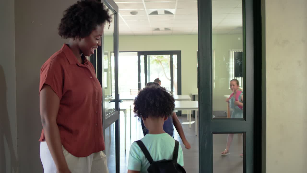African American teacher welcoming children at door guiding backpacks into classroom, copy space