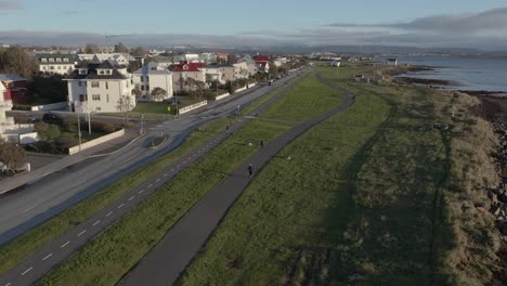 Gente-Que-Usa-La-Acera-En-La-Costa-Cubierta-De-Hierba-De-Islandia-En-Los-Suburbios-De-Reykjavik,-Antena