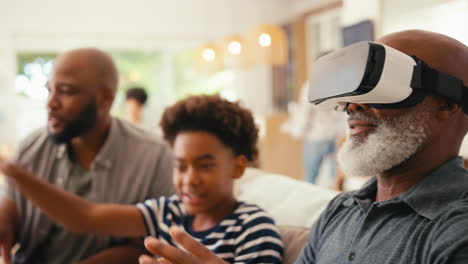 grandfather wearing vr headset as multi-generation male family sit on sofa at home together