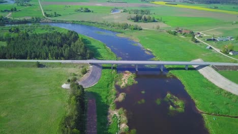 Vista-Aérea-De-Un-Río-Venta-En-Un-Día-Soleado-De-Verano,-Exuberantes-árboles-Y-Prados-Verdes,-Hermoso-Paisaje-Rural,-Disparo-De-Drones-De-Gran-Angular-Que-Avanza-Sobre-El-Puente-De-Hormigón-Blanco