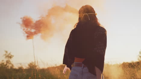 two female friends camping at music festival running through field with smoke flares