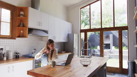 woman drinking coffee while having a video chat on her laptop at home